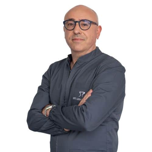 Bald man with glasses wearing a dark zippered jacket, standing with arms crossed and looking at the camera against a white background, representing the Dentalmed Group.