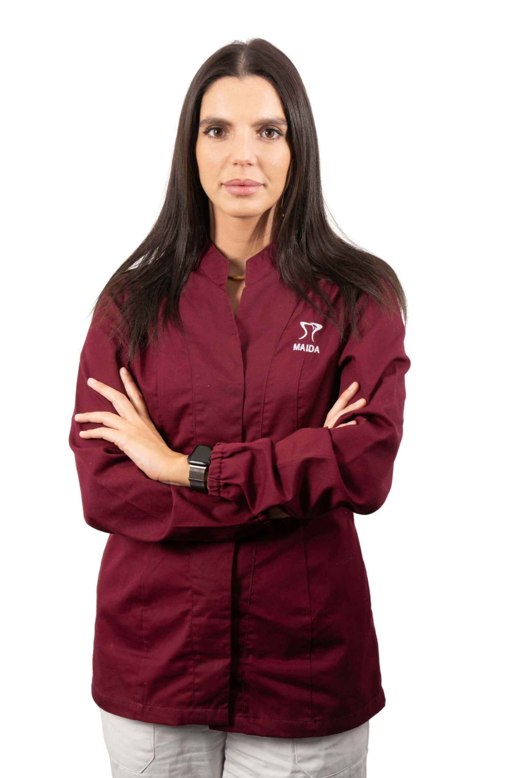 Woman in a burgundy Dentalmed Group uniform with arms crossed, wearing a watch, standing against a white background.